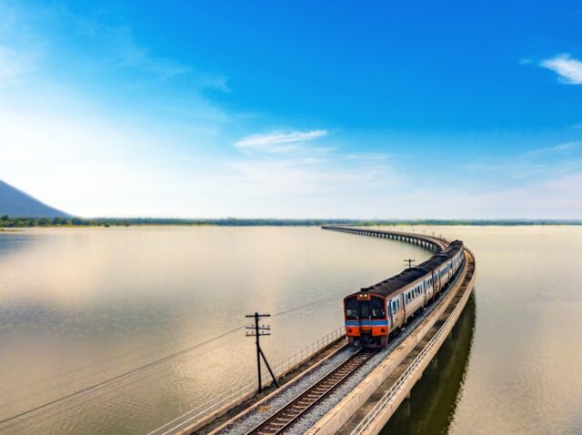 Aerial view of amazing Thailand travel train look like floating above the lake of Pa Sak Jolasid dam with blue sky. Unseen Train is running on the railway bridge over the reservoir at Lopburi Thailand